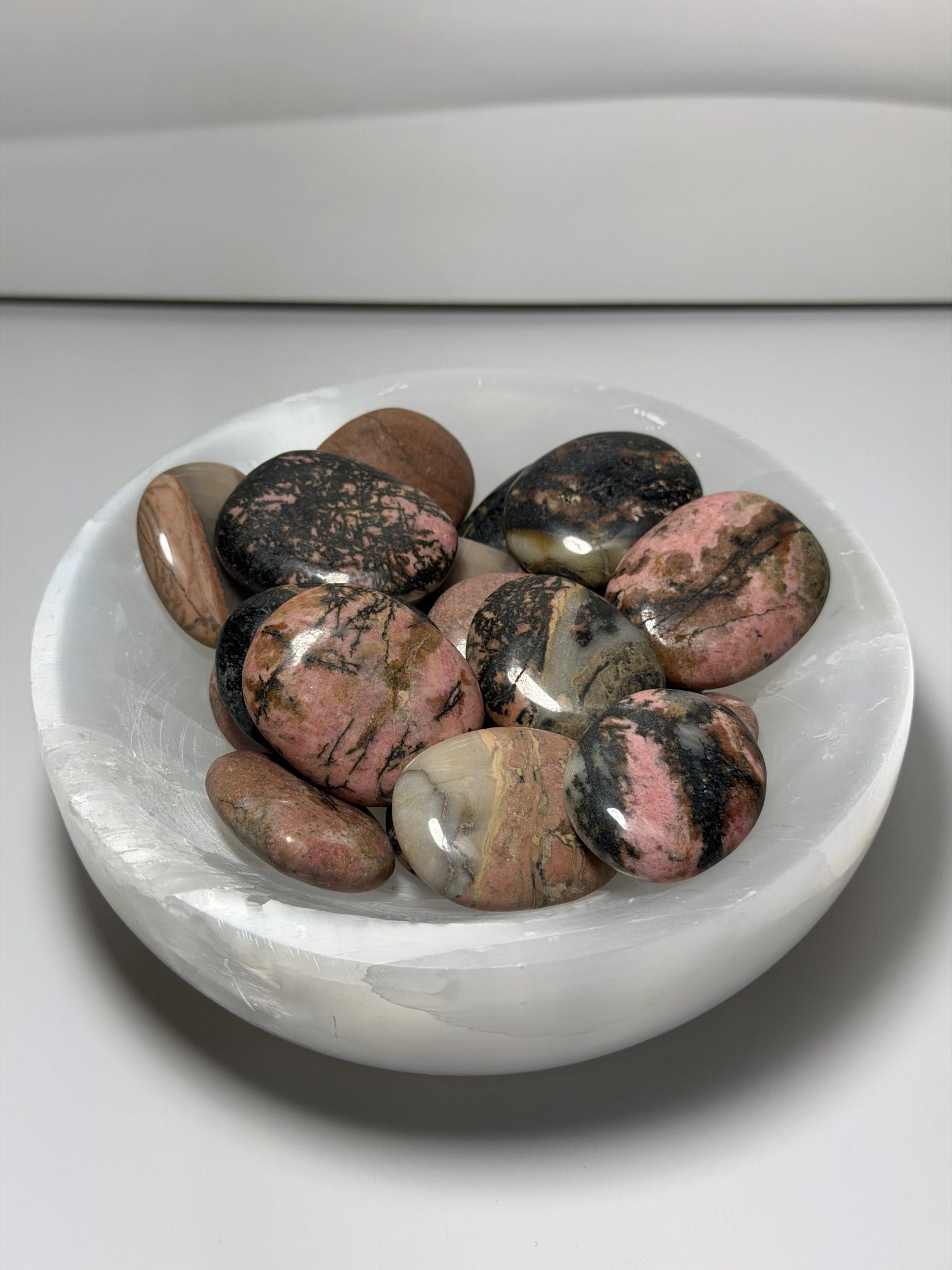 Rhodochrosite polished palmstones in white crystal bowl