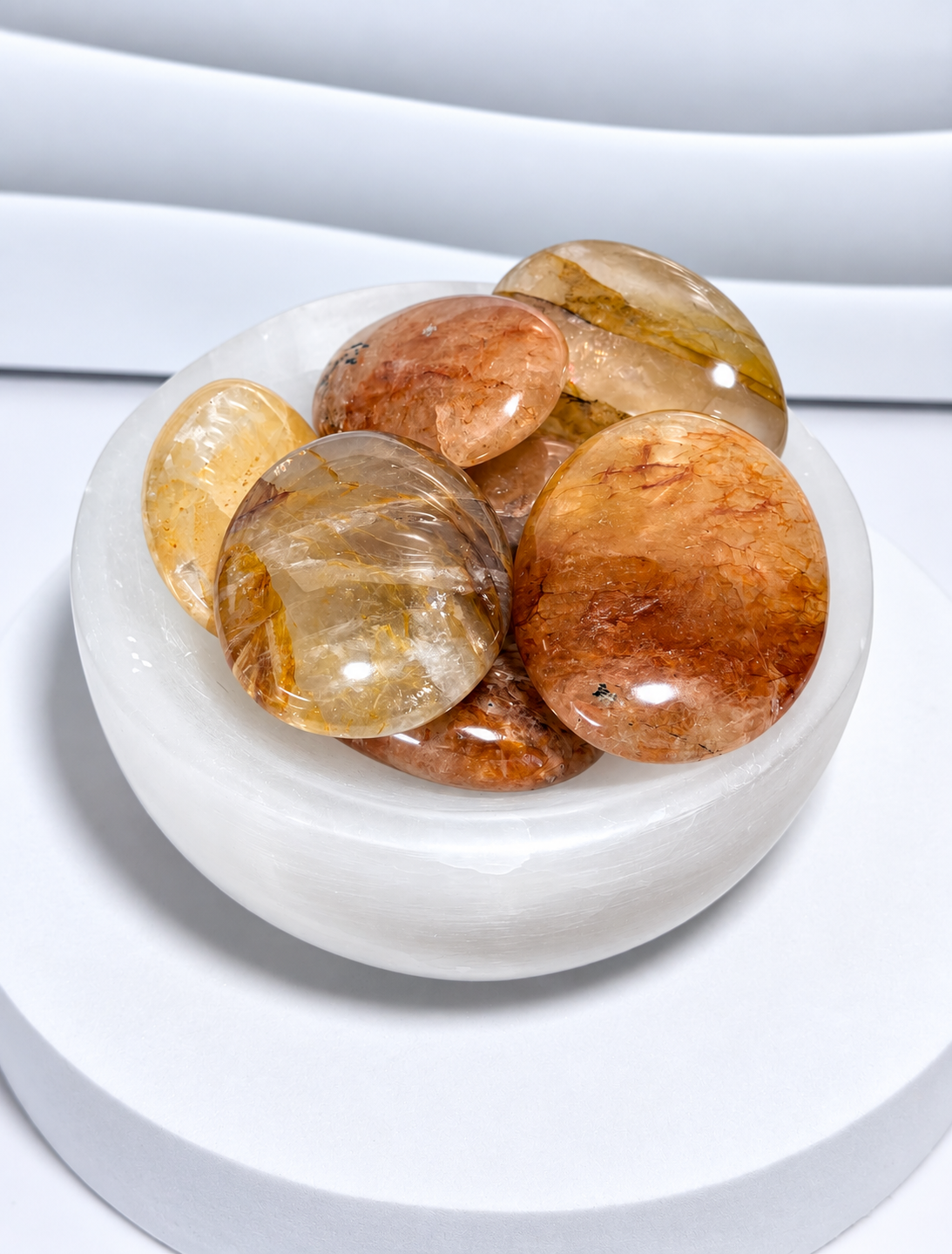 Golden Healer Quartz palm stones in honey, amber, peach and golden tones displayed in a white crystal bowl