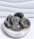 Purple Flash Labradorite palm stones with gray, charcoal, purple, blue, pink and gold iridescent flashes in a white crystal bowl