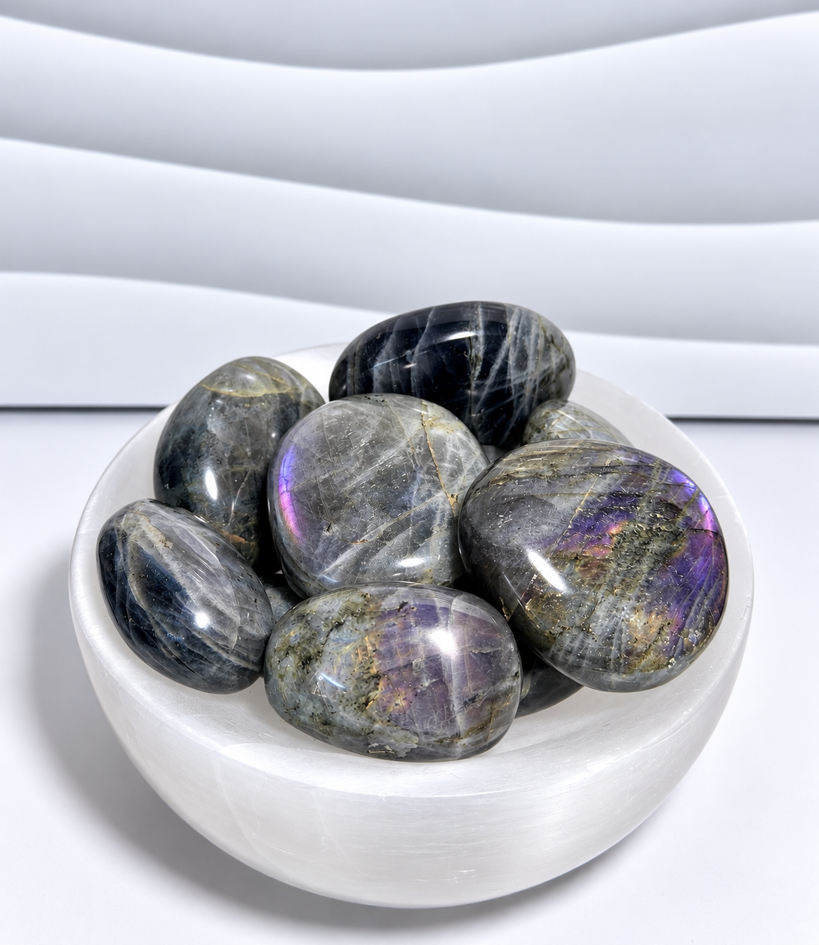 Purple Flash Labradorite palm stones with gray, charcoal, purple, blue, pink and gold iridescent flashes in a white crystal bowl